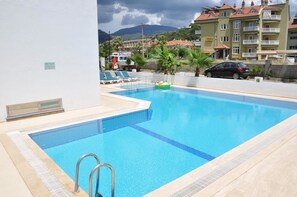 A swimming pool with a metal ladder, lounge chairs, and a small inflatable raft. - Sofi Apart (Marmaris)