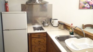 Une cuisine de taille modeste, dotée d’une hotte en acier inoxydable, d’un réfrigérateur blanc, de meubles de rangement en bois, d’un évier avec un égouttoir et d’un tableau accroché au mur.