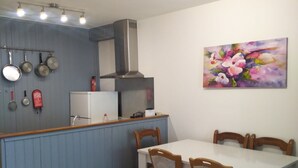 Une cuisine compacte avec un coin repas, comprenant une table blanche et des chaises en bois, un mur d’accent bleu et un porte-ustensiles suspendu.
