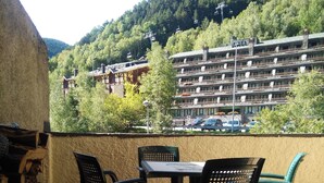 Une terrasse avec une table et des chaises, donnant sur une colline boisée et un immeuble à plusieurs étages doté de balcons.