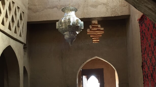 An interior with a high ceiling, a hanging chandelier, a patterned rug, and a view through an archway. - Zaid House (Taouz)