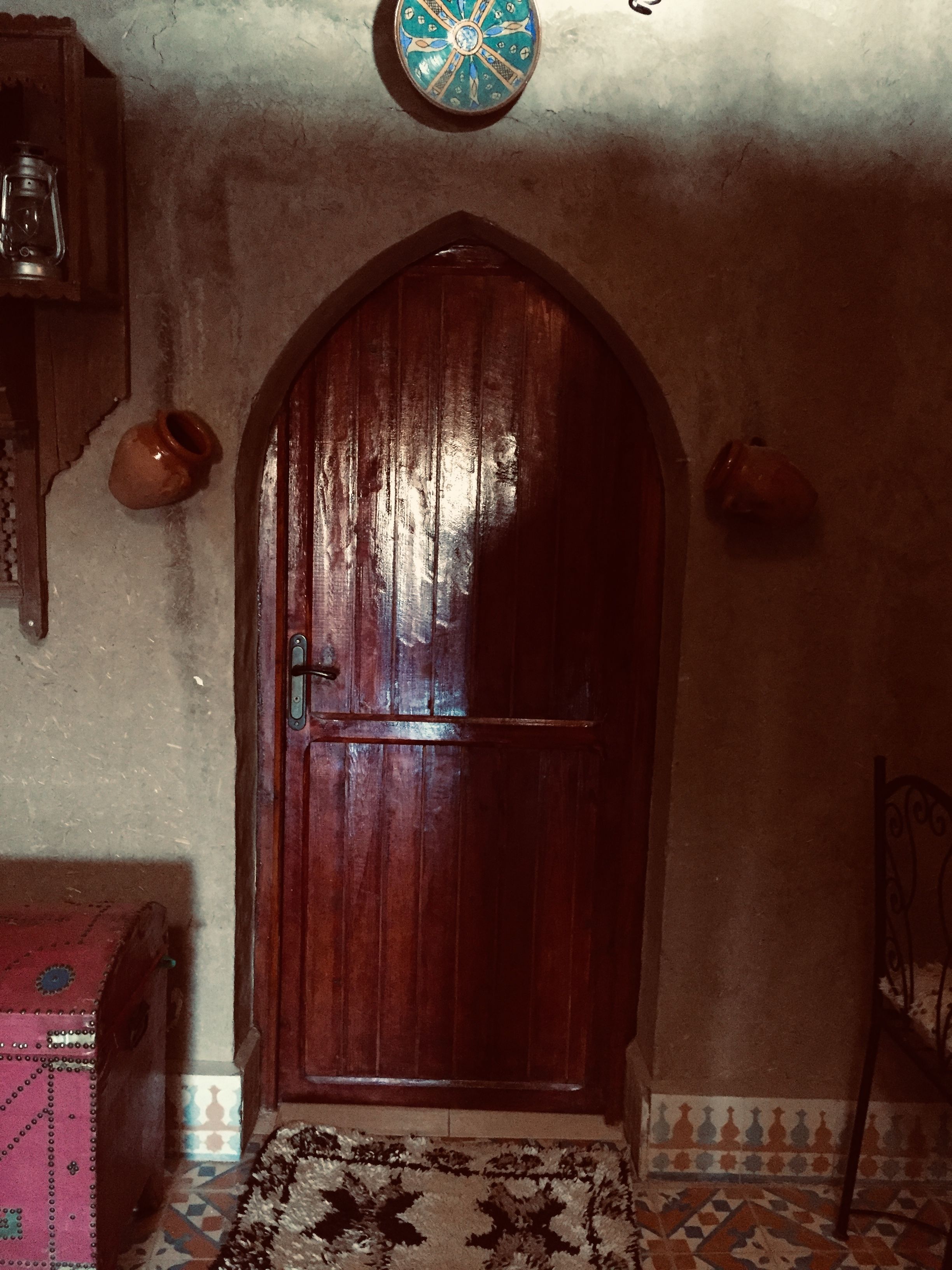 A wooden door with a decorative arch, a patterned rug, and a wall-mounted clock.