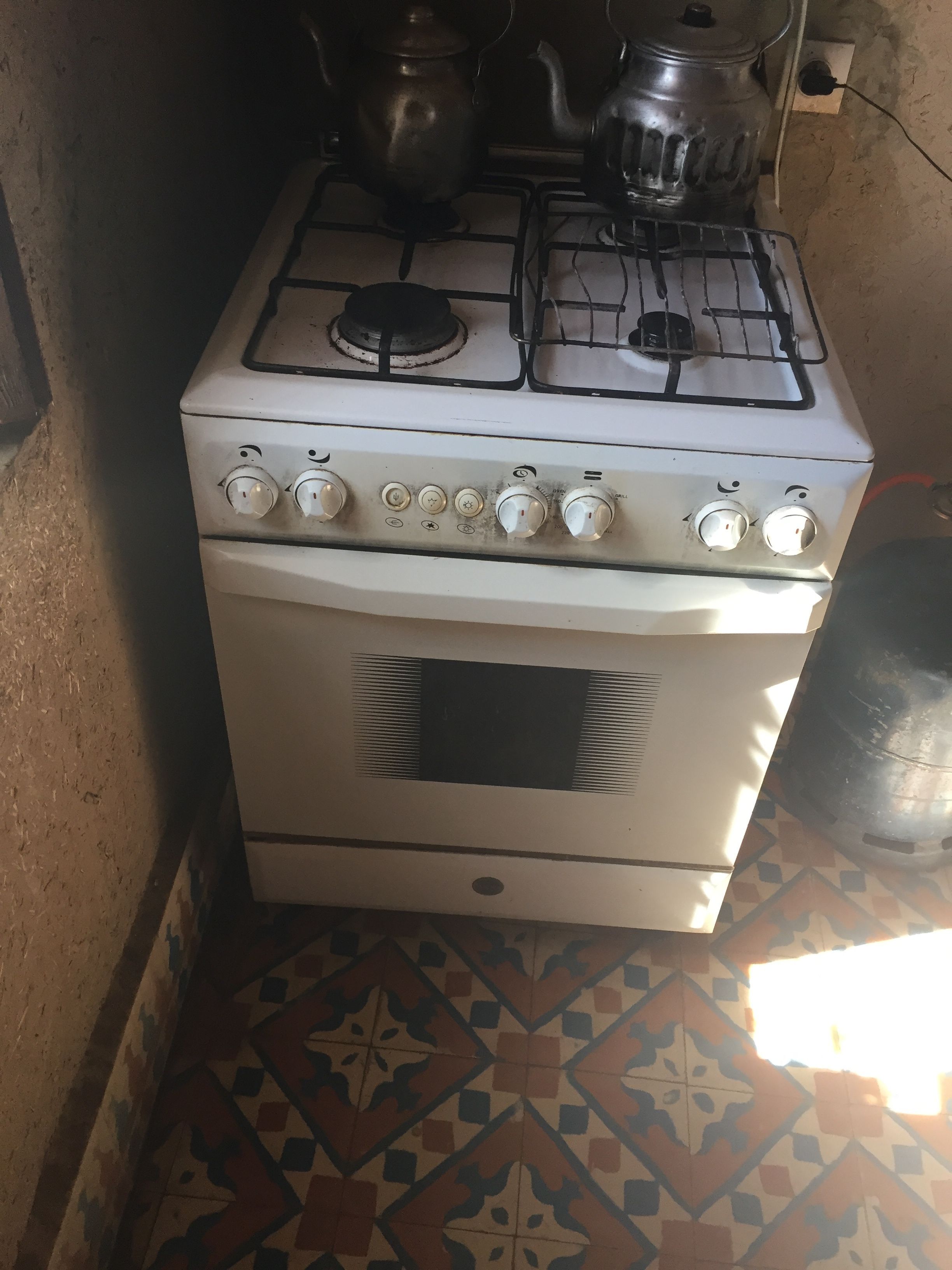 A white gas stove with four burners and a range hood, situated in a kitchen with patterned tile flooring.