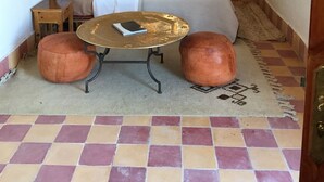 A room with a bed, a small table with a book, two ottomans, a hanging lantern, and a patterned rug. - Zaid House (Taouz)