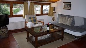 A cozy living room with a wooden ceiling, a sofa, a chair, a coffee table with a wine bottle, and a television. - Apartment Mola 19 (Arinsal)