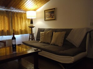Un salón acogedor con un sofá, una lámpara y una botella de vino sobre una mesa.