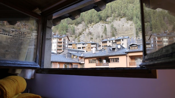 A view from a window overlooking a mountain village with traditional buildings and a forested hillside. - Apartment Mola 19 (Arinsal)