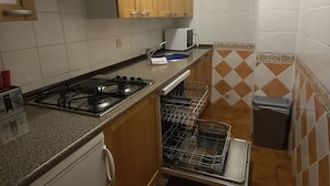 Una cocina compacta con armarios de madera, estufa a gas, microondas y lavavajillas.