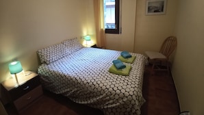 Un dormitorio con una cama, dos lámparas de noche, una silla, una ventana y un cuadro en la pared.