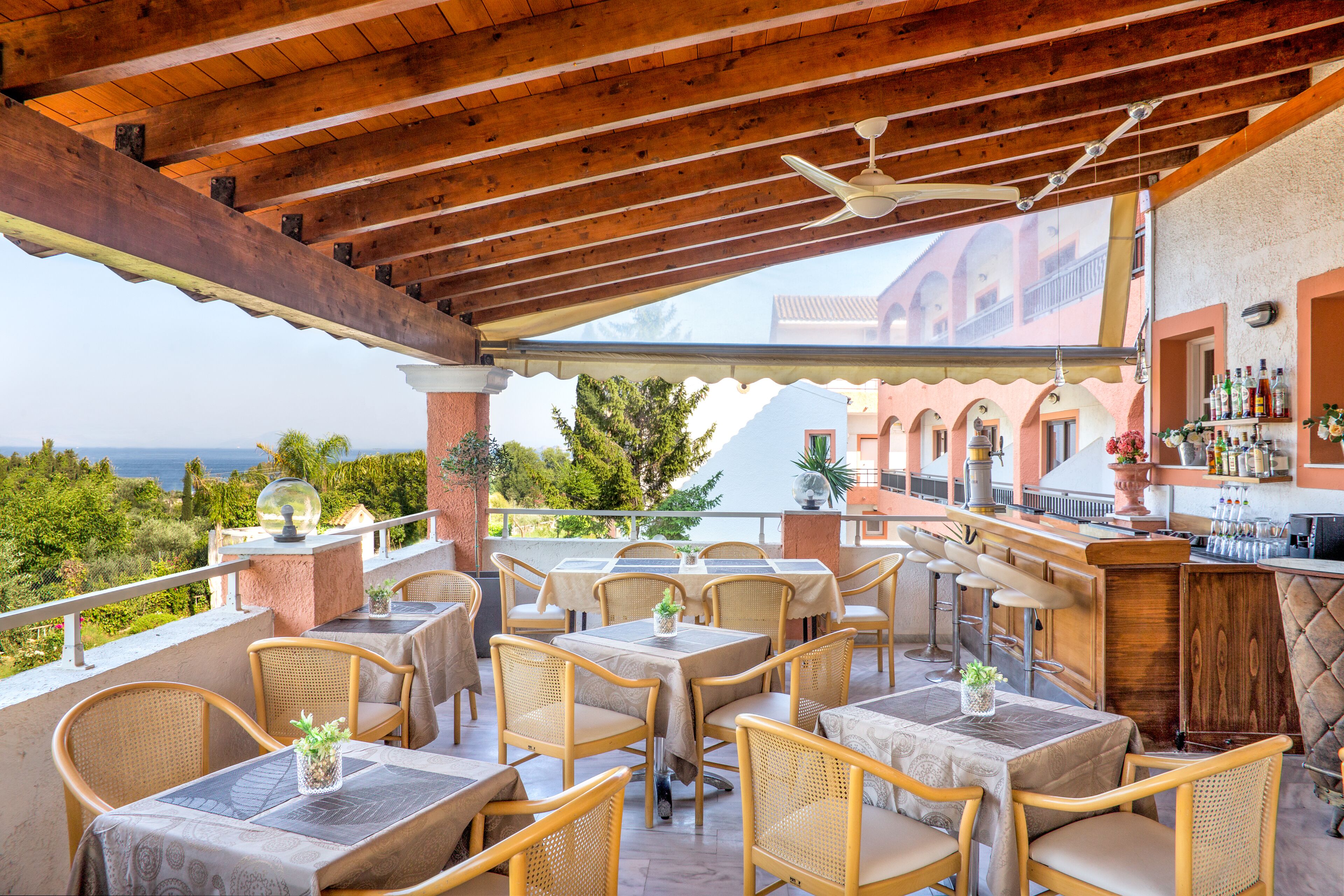 Eine Außenpatio mit Holztischen und -stühlen, einer Bar und Meerblick.