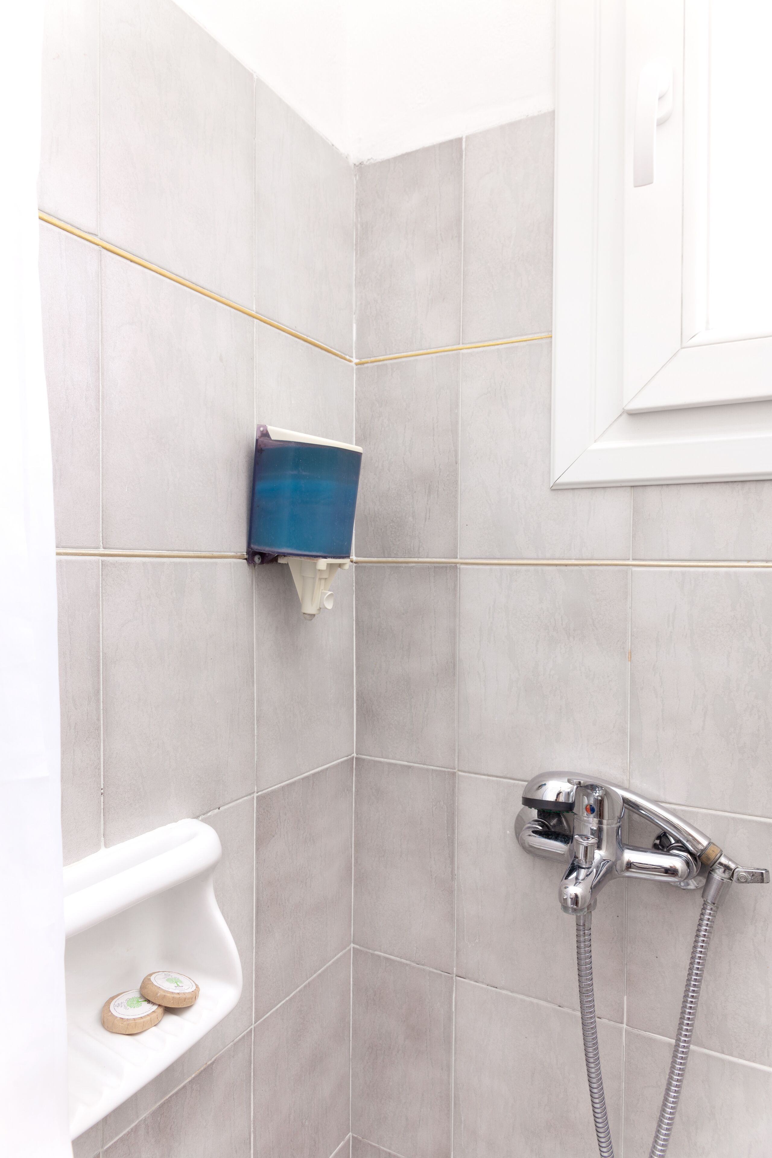 A bathroom with grey tiles, a white sink with soap, and a shower with a chrome faucet.