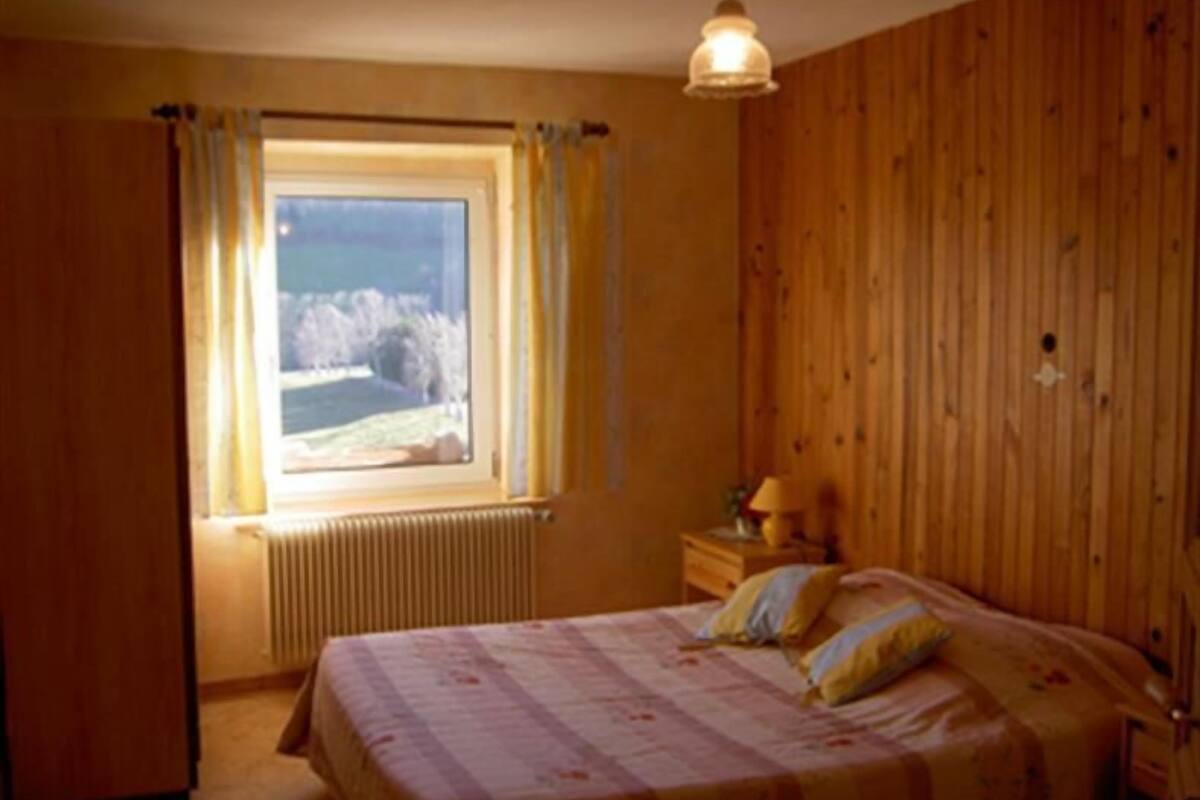 A bedroom with a bed, a nightstand, a lamp, a window with curtains, and a view of the outdoors.