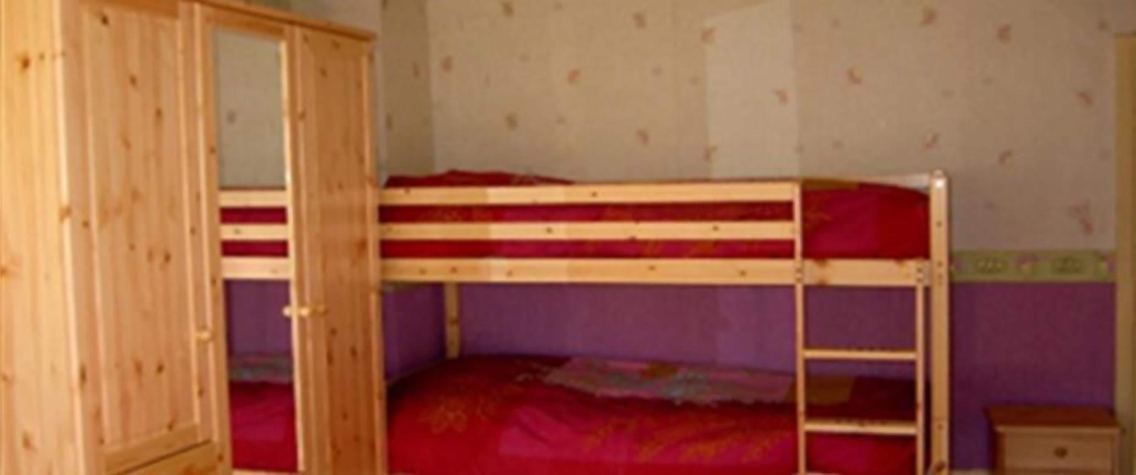 A bunk bed room with a wooden wardrobe and a purple wall.