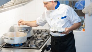 A chef in a professional kitchen with stainless steel appliances and white tiled walls.