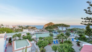 A rooftop pool area with lounge chairs, a small pool, and a view of the sea and a rocky outcrop.