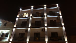 A multi-story hotel with a well-lit facade, a visible entrance with steps, and a parked car in front. - Rivendell Umbrella Collections  (Tbilisi)
