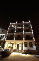 A multi-story hotel with a well-lit facade, a visible entrance with steps, and a parked car in front.