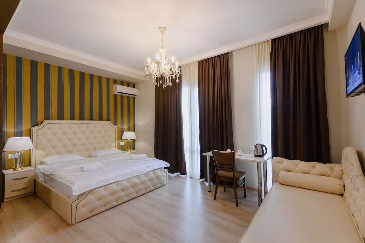 A hotel room with a bed, a desk, a chair, a sofa, a chandelier, and curtains.