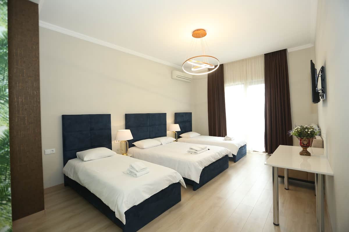 A hotel room with two beds, a desk, a flat-screen TV, and a window with curtains.