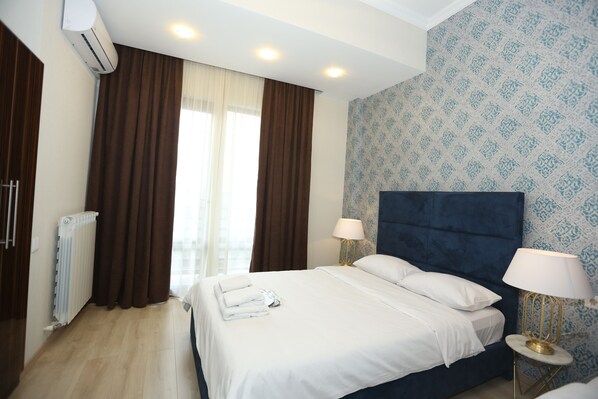 A hotel room with a large bed, two bedside lamps, a radiator, and a window with curtains.