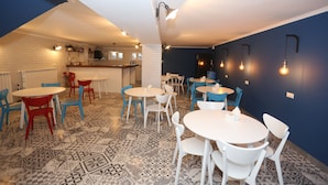 A dining area with round tables and chairs, a kitchen in the background, and patterned flooring. - Rivendell Umbrella Collections  (Tbilisi)