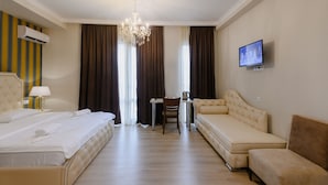 A hotel room with a bed, a sofa, a desk with a chair, a television, and a chandelier. - Rivendell Umbrella Collections  (Tbilisi)