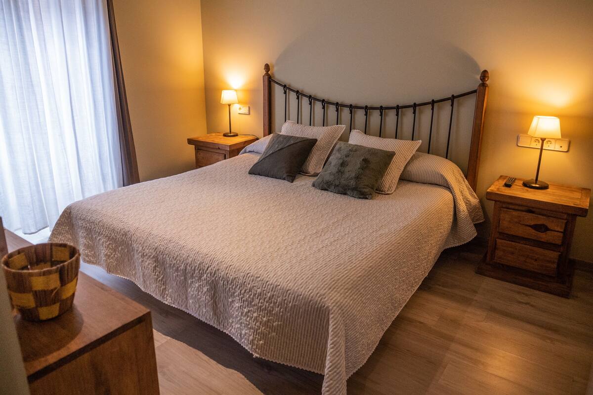 A neatly made bed with a textured blanket, two bedside lamps, and a wooden nightstand with a bowl.