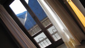 A view through a window with a metal frame, a blue building outside, and a white curtain partially covering the window. - Pèira Blanca Hotel Gastronómico (Naut Aran)