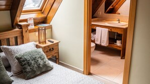A bedroom with a sloped ceiling, a skylight, a bed with pillows, a nightstand, and a view into an adjacent bathroom. - Pèira Blanca Hotel Gastronómico (Naut Aran)