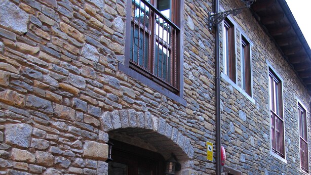 A stone building with a wooden door and multiple windows, including a balcony. - Pèira Blanca Hotel Gastronómico (Naut Aran)