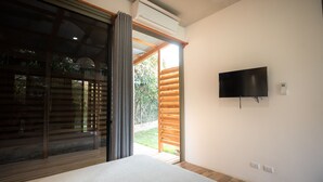 A bedroom with a bed, a TV mounted on the wall, and a sliding door leading to an outdoor area. - Congo (Nosara)