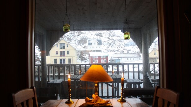 A wooden table with a lamp and candles, overlooking a snowy landscape with buildings. - Holmvik Brygge Nyksund (Oksnes)
