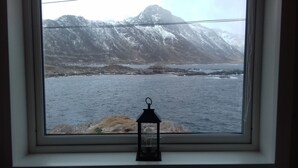 A window with a view of a mountainous landscape and a body of water. - Holmvik Brygge Nyksund (Oksnes)