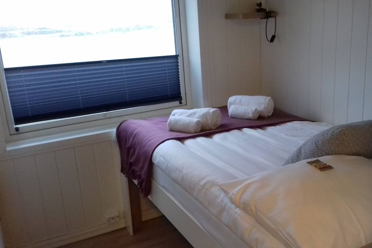 Siististi pedattu sänky, jossa on kaksi rullalle taitettua pyyhettä, harmaa tyyny ja violetti peitto.