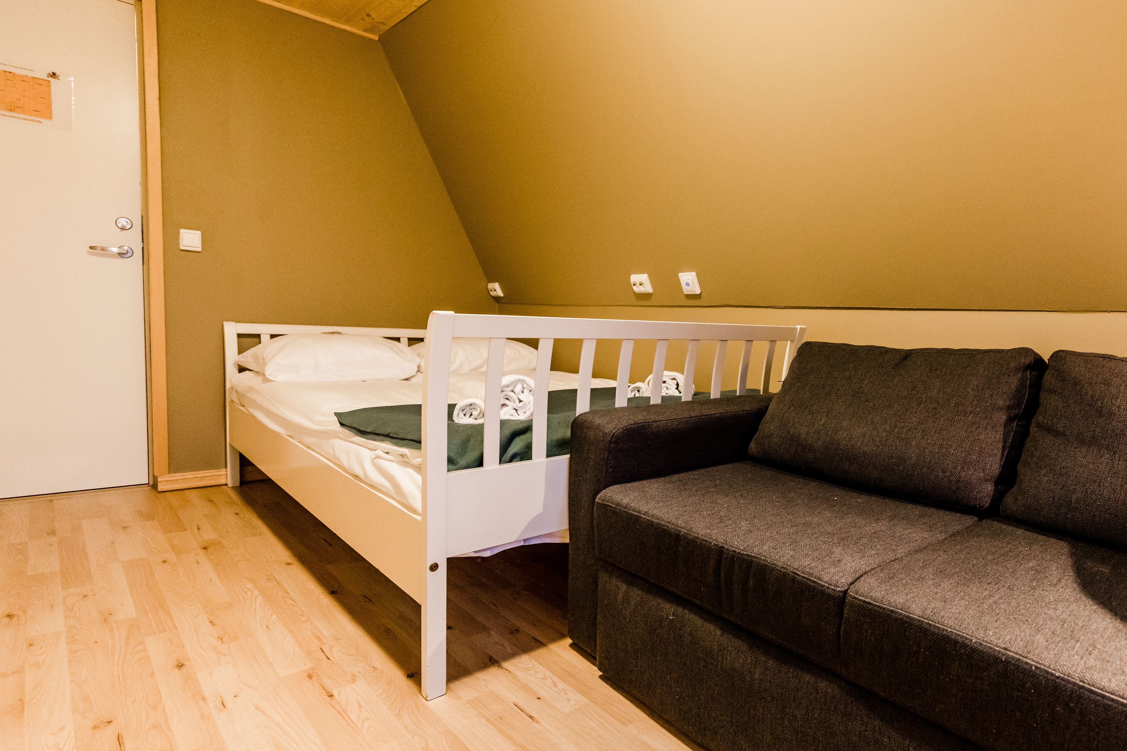 A room with a bunk bed, a dark-colored sofa, and a door with a light switch.