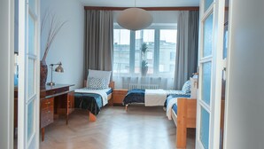 A bedroom with two beds, a desk, a chair, a hanging light fixture, and a window with curtains. - 4Culture Apart (Lodz)