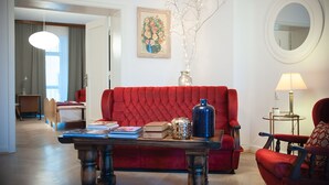 A living room with a red sofa, a coffee table with books and decorative items, a lamp, and a painting on the wall. - 4Culture Apart (Lodz)