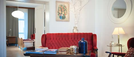 A living room with a red sofa, a coffee table with books and decorative items, a lamp, and a painting on the wall.