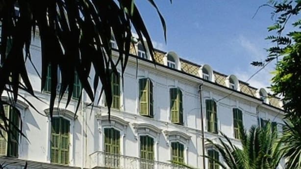 Un bâtiment avec une fontaine dans le jardin, entouré de verdure et de voitures garées.