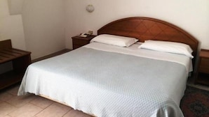 Un lit simple avec une tête de lit en bois, une table de chevet avec une lampe et un luminaire fixé au mur.