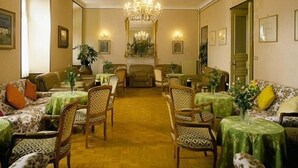 Une pièce décorée d’un lustre, avec plusieurs tables recouvertes de nappes vertes et des chaises à motifs.