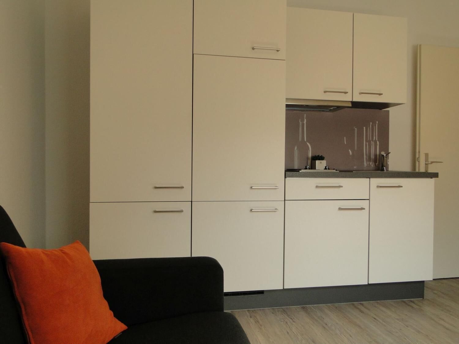 A modern kitchen with white cabinets, a black countertop, and a grey floor.