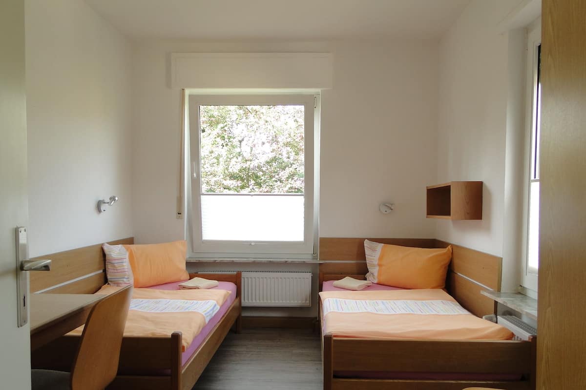 A small, clean room with two wooden beds, a window, and a radiator.