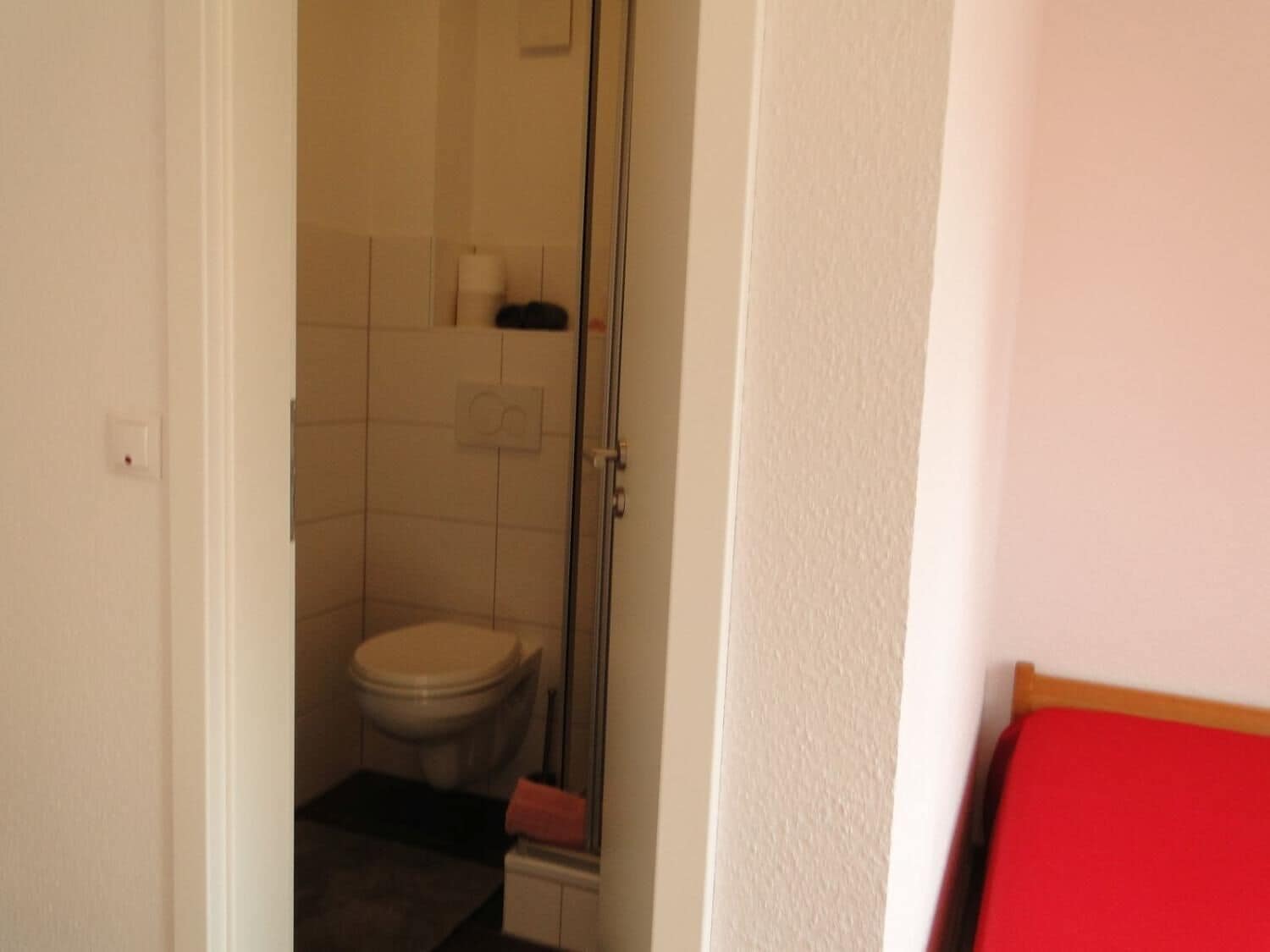 Un pasillo estrecho que conduce a un baño con inodoro, ducha y un banco rojo.