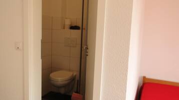 Un pasillo estrecho que conduce a un baño con inodoro, ducha y un banco rojo.
