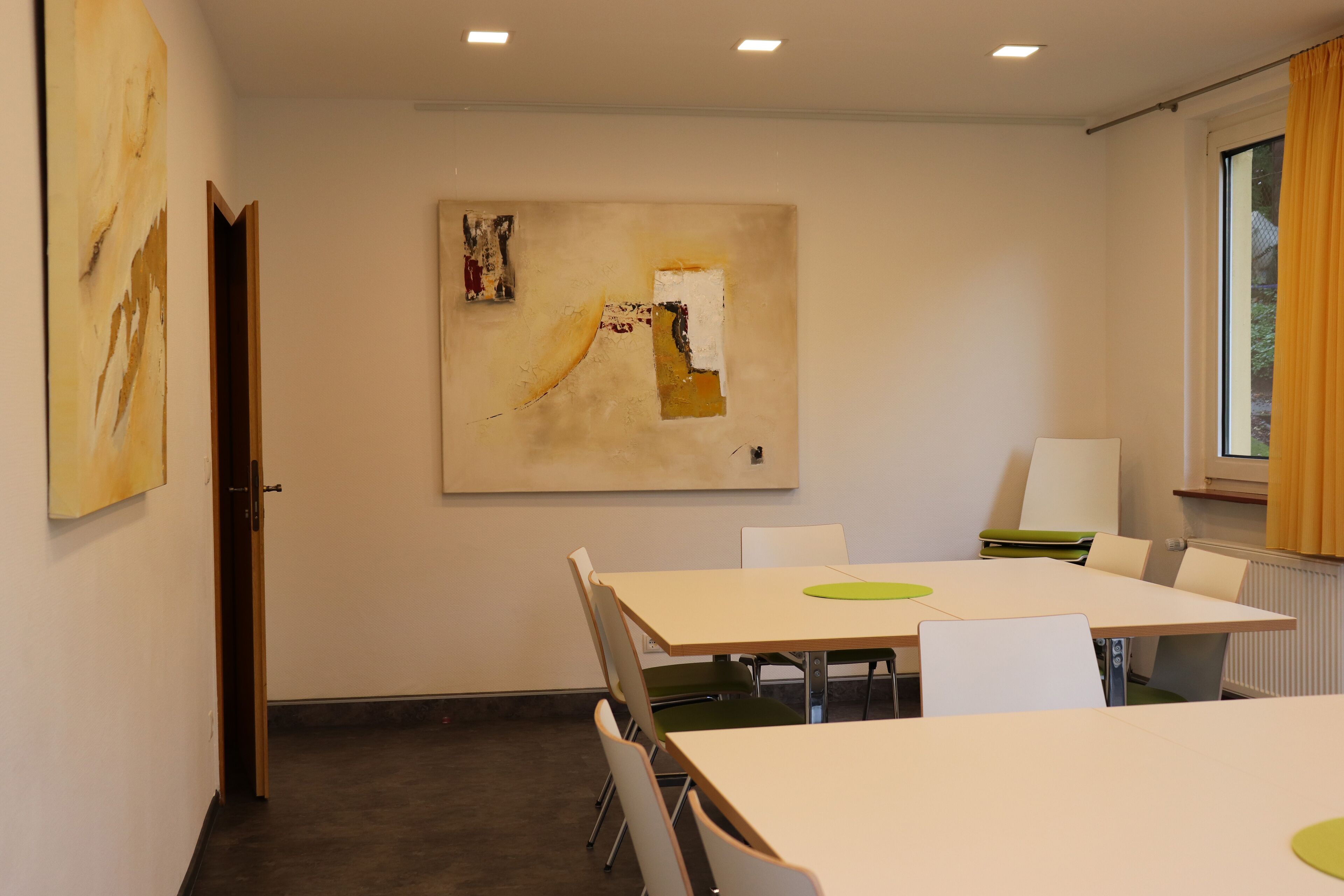 A conference room with a large table, white chairs, and a painting on the wall.