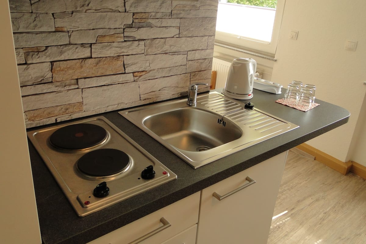 A kitchen with a stone backsplash, stainless steel sink, double electric stove, and a coffee maker.