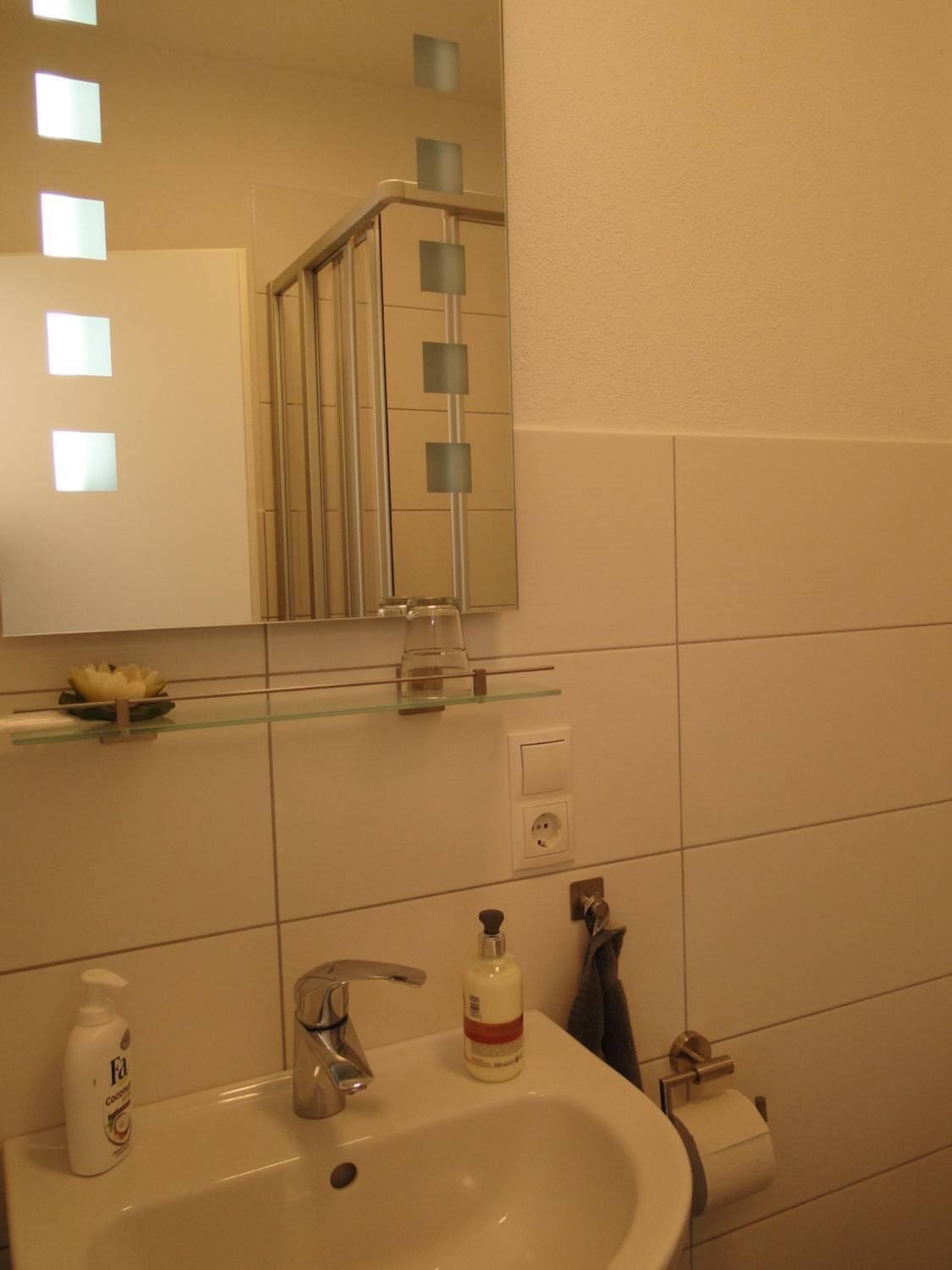 Bany amb un lavabo blanc, un mirall, una prestatgeria de vidre amb articles de tocador i un suport per a tovalloles.