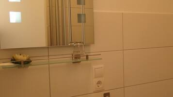 Bany amb un lavabo blanc, un mirall, una prestatgeria de vidre amb articles de tocador i un suport per a tovalloles.