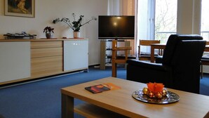 Een moderne woonkamer met een flatscreen televisie, houten meubels, een eethoek en een groot raam.